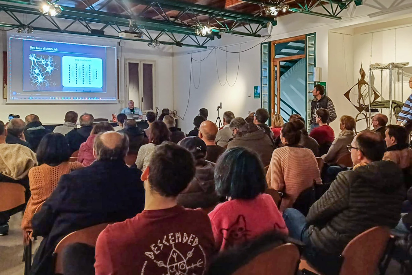 Sergio Bertolini durante un seminario di public speaking sull'intelligenza artificiale: proiezione delle slide, Sergio che parla e il pubblico in sala